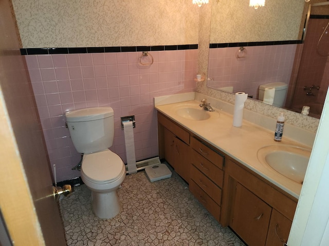 bathroom featuring wallpapered walls, double vanity, toilet, and a sink