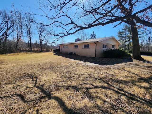 view of side of home featuring brick siding, a chimney, and a lawn