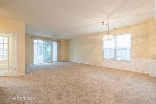 empty room with a decorative wall, carpet, a wainscoted wall, and ceiling fan with notable chandelier