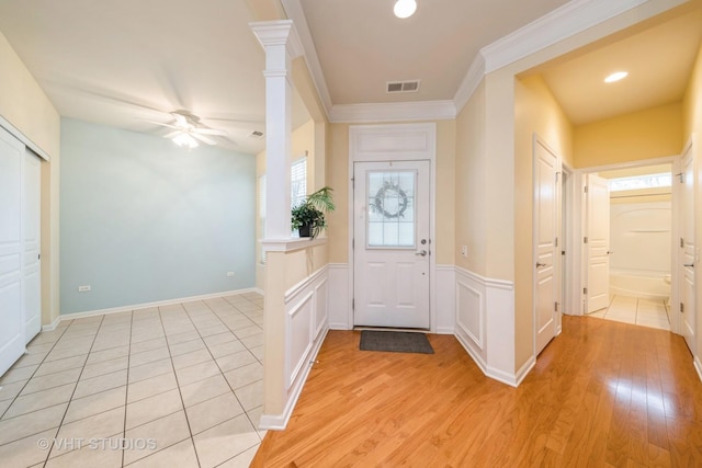 foyer featuring a wainscoted wall, visible vents, decorative columns, ceiling fan, and light wood-style floors