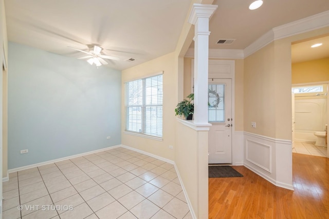 entrance foyer with visible vents, a wainscoted wall, a ceiling fan, crown molding, and ornate columns