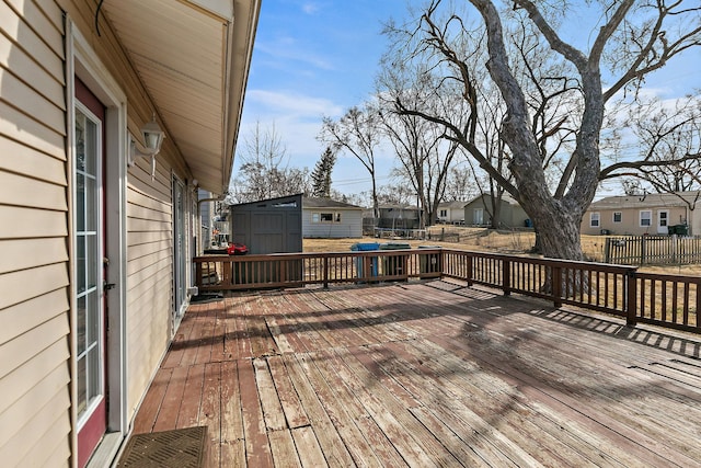 wooden deck featuring a trampoline, fence, a residential view, a storage shed, and an outdoor structure