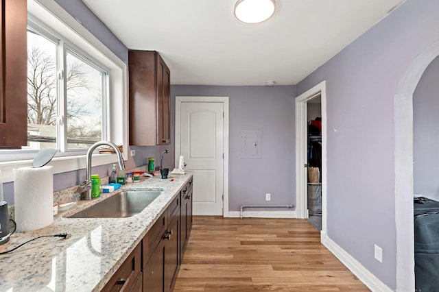 kitchen with arched walkways, dark brown cabinetry, light wood-style flooring, a sink, and baseboards