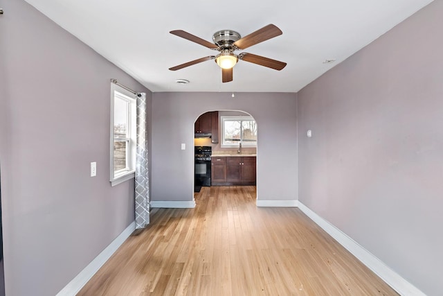 unfurnished room with arched walkways, light wood-style floors, a sink, ceiling fan, and baseboards