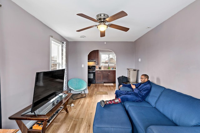 living area featuring a healthy amount of sunlight, light wood-style flooring, arched walkways, and a ceiling fan