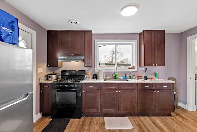 kitchen featuring black range with gas cooktop, visible vents, freestanding refrigerator, under cabinet range hood, and a sink