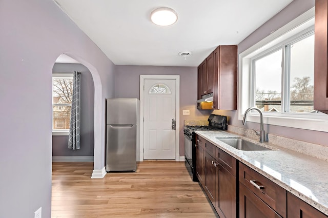 kitchen featuring under cabinet range hood, a sink, visible vents, freestanding refrigerator, and black gas range oven