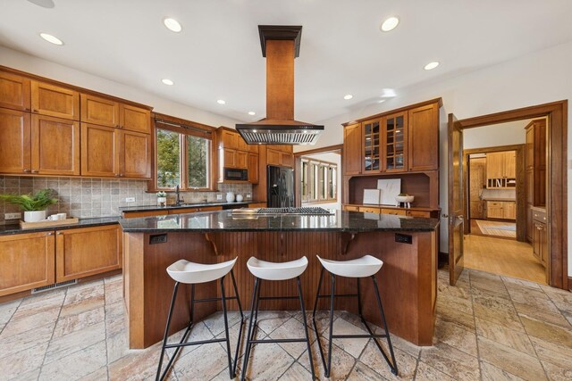 kitchen featuring island exhaust hood, stone tile flooring, visible vents, a kitchen island, and black appliances