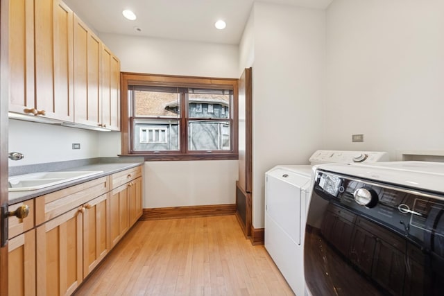 clothes washing area with cabinet space, light wood-style flooring, a sink, separate washer and dryer, and baseboards