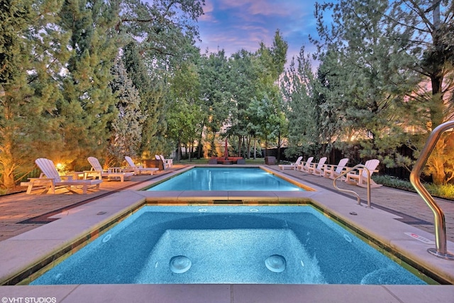 pool at dusk featuring a patio area, an outdoor pool, and an in ground hot tub