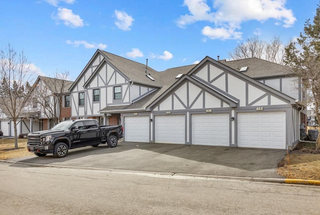 tudor-style house featuring a garage, aphalt driveway, a shingled roof, and stucco siding