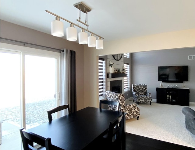 carpeted dining area with a fireplace, visible vents, and track lighting