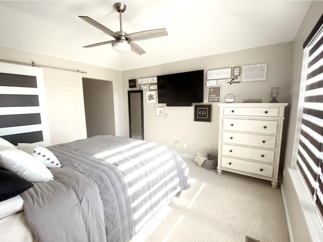 bedroom with light colored carpet, ceiling fan, and a barn door