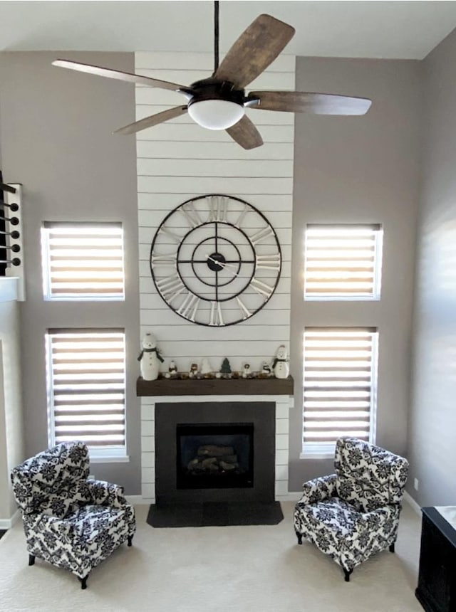 carpeted living area with a ceiling fan, a fireplace, and a high ceiling