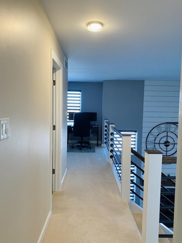 hall featuring carpet floors, baseboards, visible vents, and an upstairs landing