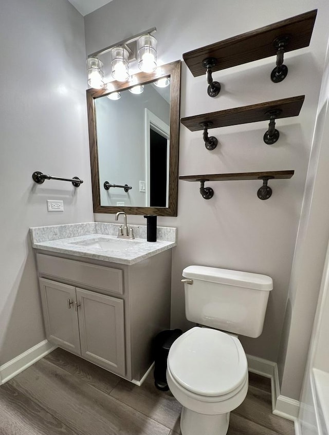 bathroom featuring toilet, baseboards, wood finished floors, and vanity