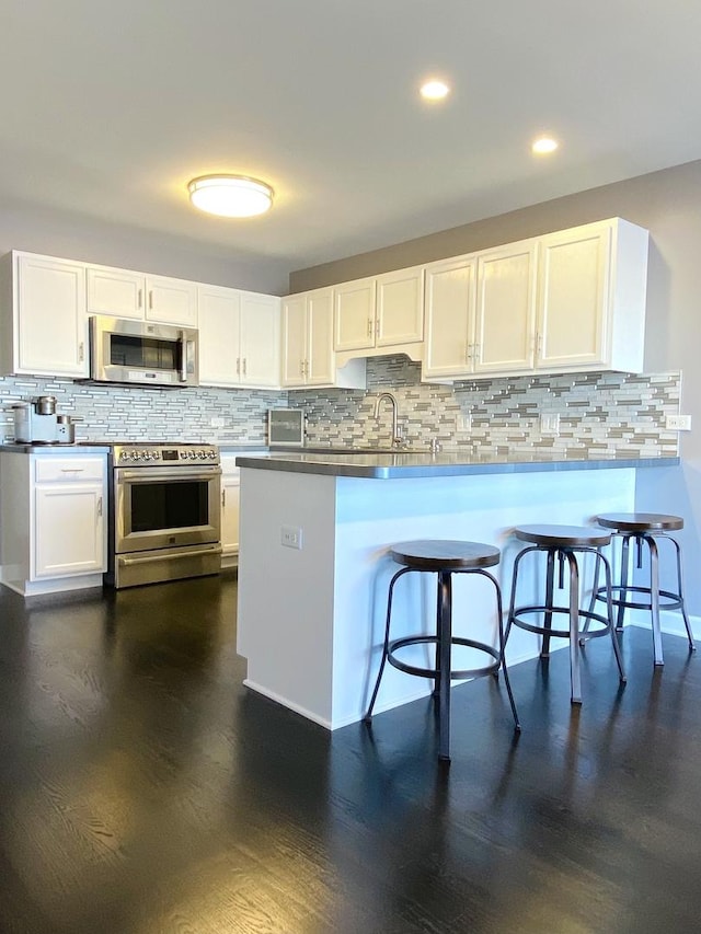 kitchen with white cabinets, a breakfast bar area, dark wood-style flooring, a peninsula, and stainless steel appliances