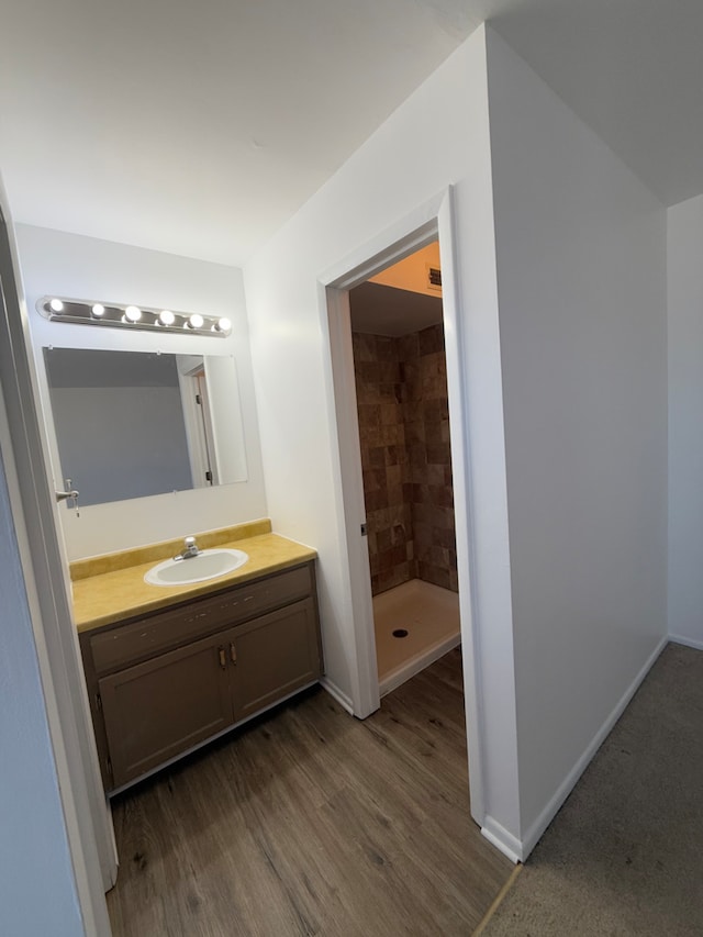 bathroom featuring baseboards, a tile shower, wood finished floors, and vanity