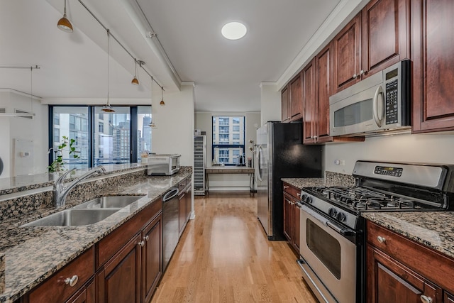 kitchen featuring stainless steel appliances, a sink, light wood-style floors, hanging light fixtures, and dark stone countertops