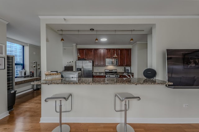 kitchen featuring appliances with stainless steel finishes, a kitchen breakfast bar, dark stone countertops, and wood finished floors