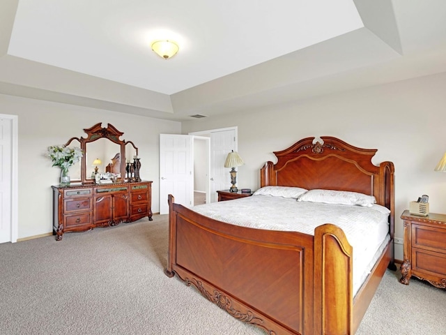 bedroom with a tray ceiling, light carpet, visible vents, and baseboards