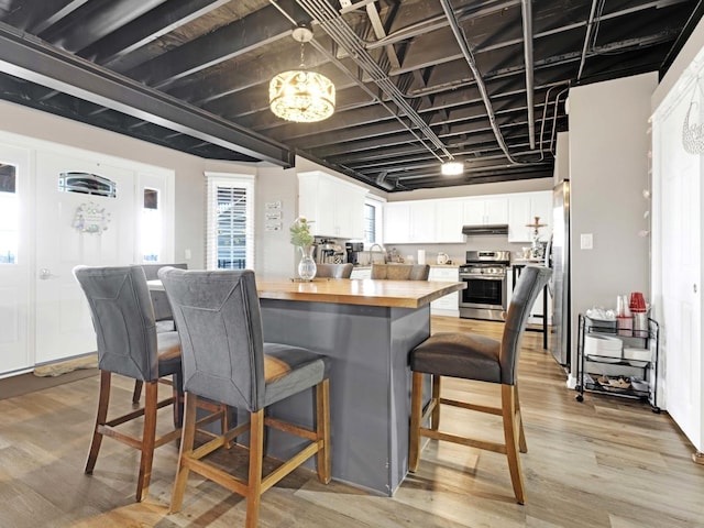 kitchen featuring butcher block countertops, a breakfast bar, stainless steel appliances, light wood-style floors, and white cabinetry