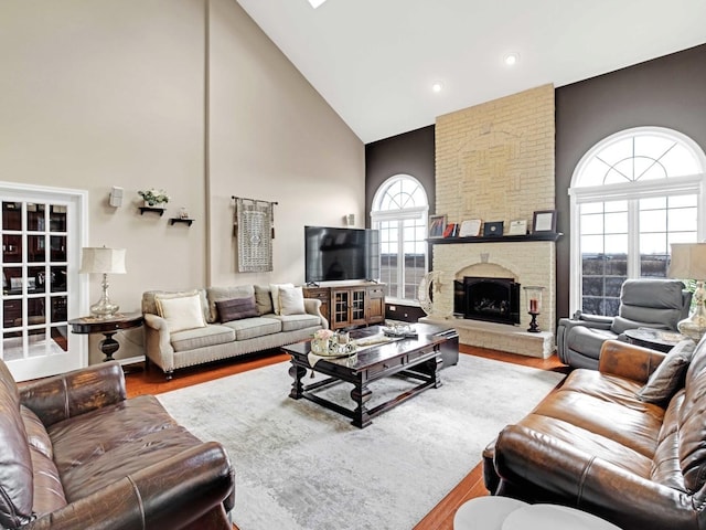 living room with high vaulted ceiling, a brick fireplace, and wood finished floors