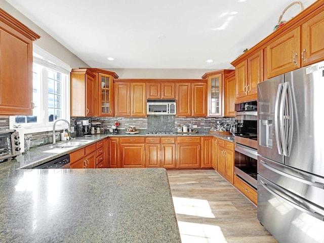 kitchen with stainless steel appliances, brown cabinetry, glass insert cabinets, and decorative backsplash