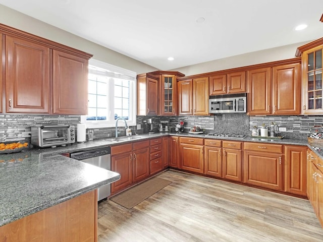 kitchen with tasteful backsplash, brown cabinets, stainless steel appliances, light wood-style floors, and a sink