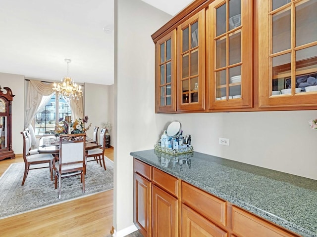 kitchen with a chandelier, light wood-style flooring, hanging light fixtures, brown cabinetry, and glass insert cabinets