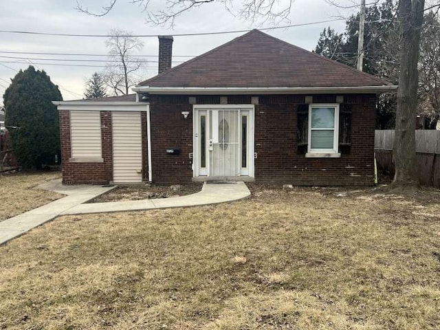 bungalow featuring brick siding, fence, a chimney, and a front lawn