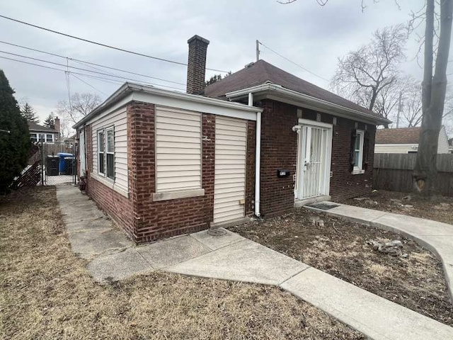 view of front of property featuring brick siding, fence, and a chimney