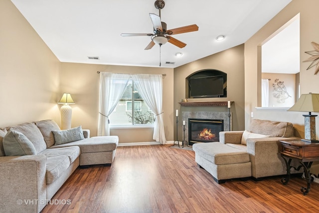 living room with a premium fireplace, wood finished floors, visible vents, and a ceiling fan