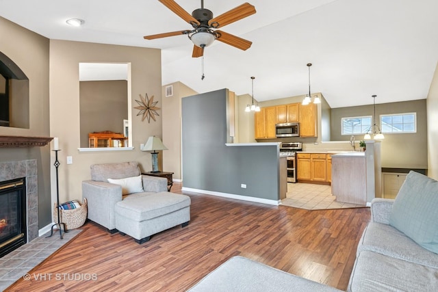 living room with light wood finished floors, visible vents, a ceiling fan, a tile fireplace, and lofted ceiling