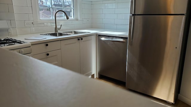 kitchen featuring white cabinets, appliances with stainless steel finishes, a sink, light countertops, and backsplash