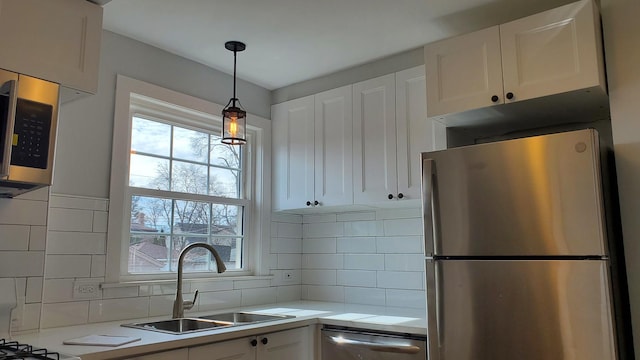 kitchen with a sink, white cabinetry, light countertops, appliances with stainless steel finishes, and pendant lighting