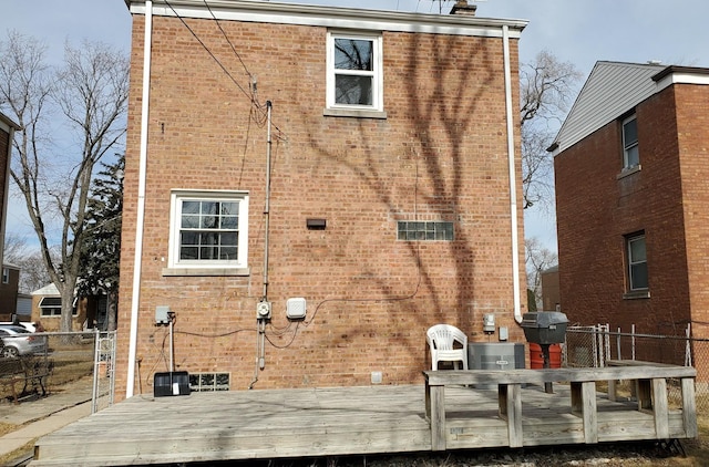 rear view of house featuring brick siding, a chimney, fence, and a wooden deck