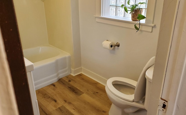 full bath featuring a bath, wood finished floors, toilet, and baseboards