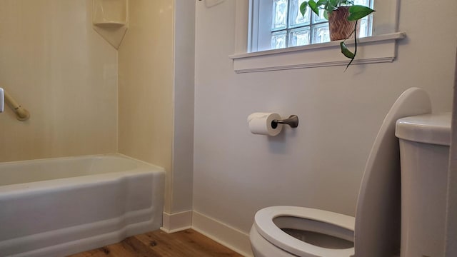 bathroom with toilet, baseboards, a washtub, and wood finished floors