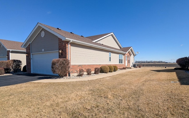 view of side of property with a garage, a lawn, brick siding, and driveway