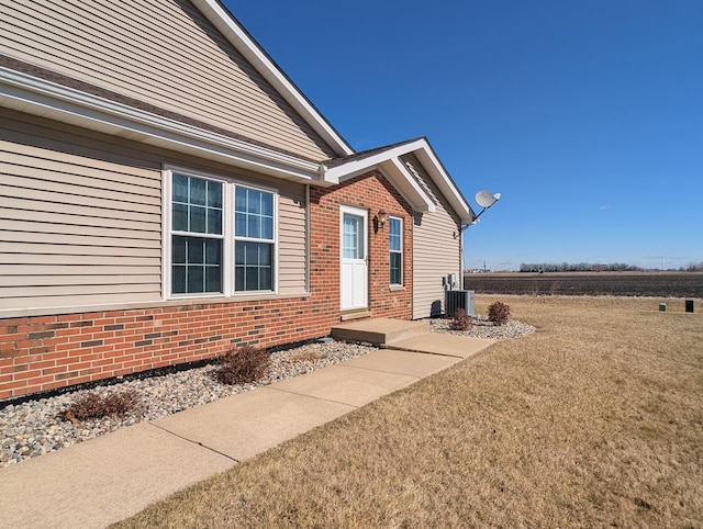 doorway to property with cooling unit, brick siding, and a lawn