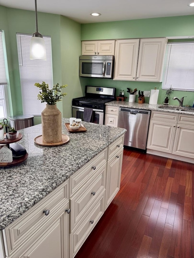 kitchen with dark wood-style floors, decorative light fixtures, stainless steel appliances, a sink, and light stone countertops