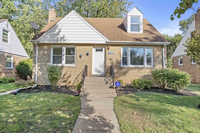 view of front of house featuring a shingled roof, a front yard, brick siding, and a chimney