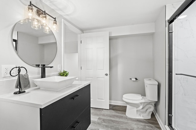 bathroom with toilet, a stall shower, vanity, wood finished floors, and baseboards