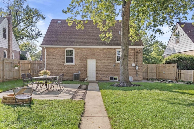 rear view of property featuring brick siding, a patio, a lawn, a fenced backyard, and a fire pit