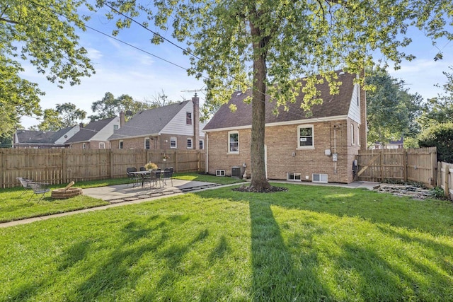 back of property with a fenced backyard, central AC, brick siding, a yard, and a patio area