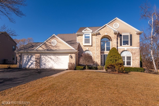 traditional-style home featuring an attached garage, driveway, brick siding, and a front yard