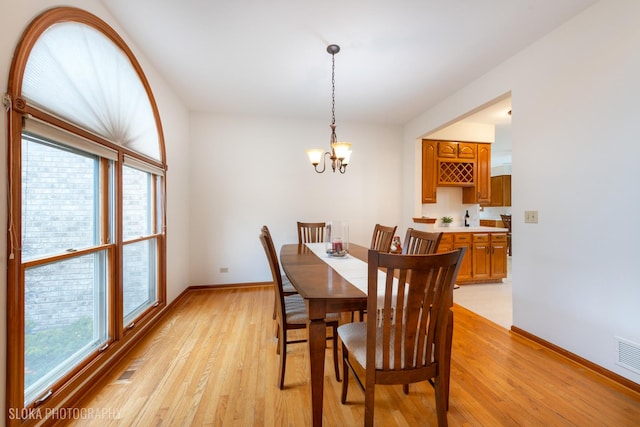 dining space featuring baseboards, visible vents, light wood finished floors, and an inviting chandelier