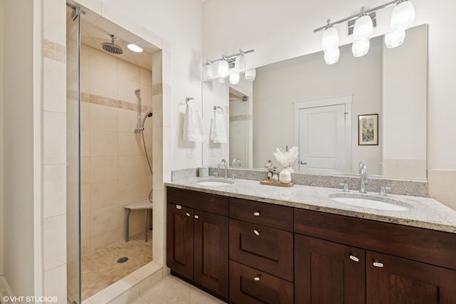 bathroom with tile patterned flooring, tiled shower, a sink, and double vanity