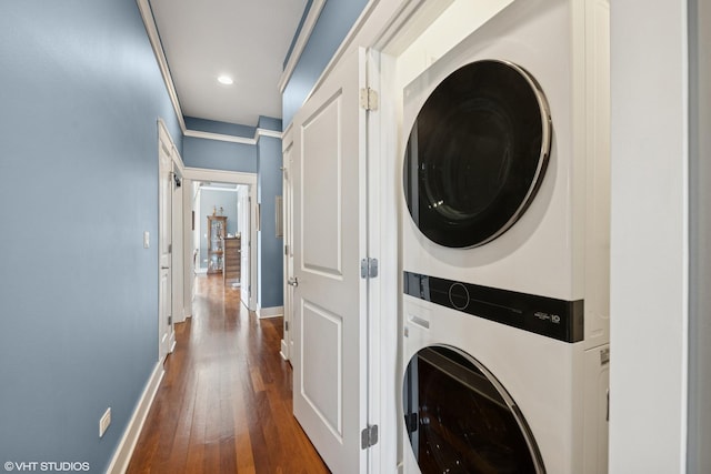 washroom with dark wood-type flooring, stacked washer and clothes dryer, baseboards, and laundry area